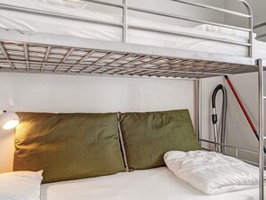Una cama individual con estructura metálica, una litera abajo y una lámpara de noche.