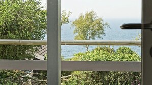 A view through a window with a wooden railing, overlooking a body of water and greenery. - 6 Person Holiday Home in Hasle (Hasle)