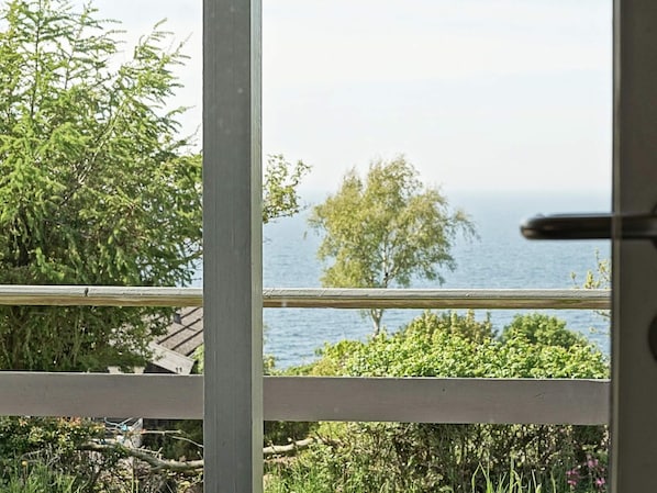 Vista pela janela, com corrimão de madeira, sobre a água e vegetação.