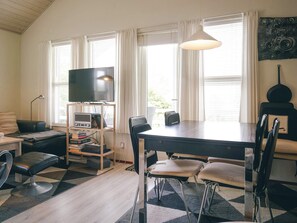 Una sala moderna con una televisión de pantalla plana, una mesa de comedor con sillas, un sofá, una mesa de centro y una estantería.