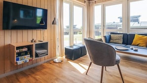 A modern living room with a flat-screen TV, wooden shelves, a floor lamp, and a sofa with cushions. - 8 Person Holiday Home in Faaborg-by Traum (Faaborg)