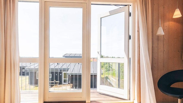 A room with a wooden floor, a table with two ceramic cups, and a sliding glass door leading to an outdoor area with a patio and a building in the background. - 8 Person Holiday Home in Faaborg-by Traum (Faaborg)
