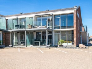 A modern building with a glass facade, outdoor seating area, and a parking lot.