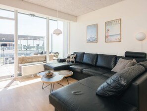 A modern living room with a black leather sofa, a round coffee table, and a large window offering a view of the outside.