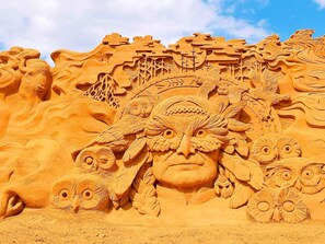En detaljerad sandskulptur som föreställer ett ansikte med flera ögon och en huvudbonad.