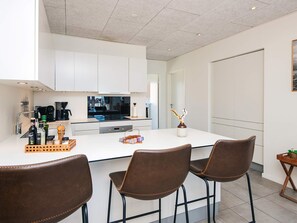 A modern kitchen with white cabinets, a central island with chairs, and a coffee machine.