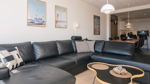 Una sala de estar moderna con un sofá de cuero negro, una mesa de centro de madera y dos cuadros en la pared.
