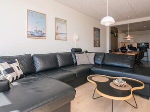 A modern living room with a black leather sofa, a wooden coffee table, and two framed pictures on the wall. - 5 Star Holiday Home in Ringkobing (Ringkobing)