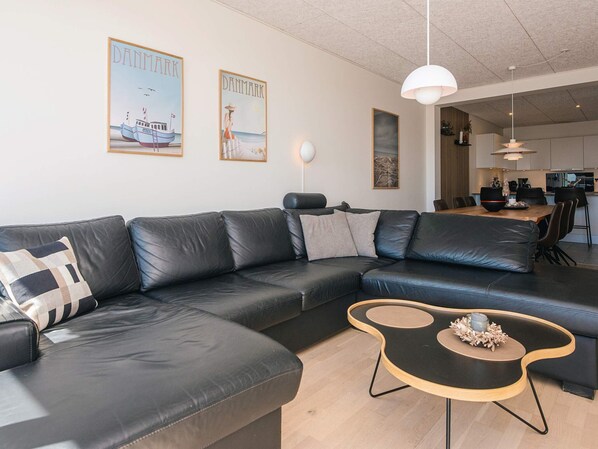 Una sala de estar moderna con un sofá de cuero negro, una mesa de centro de madera y dos cuadros en la pared.