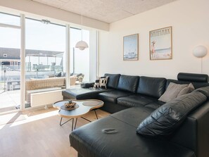 A modern living room with a black leather sofa, a small coffee table, and a view through large windows.