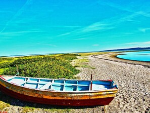 En båt ligger vid en strand med småsten, och i bakgrunden syns en sjö och en skog.