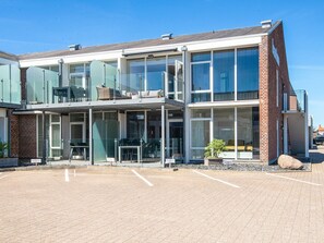A modern building with a glass facade, outdoor seating area, and a parking lot. - 5 Star Holiday Home in Ringkobing (Ringkobing)