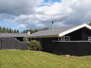 En svart träbyggnad med ett sluttande tak, en skorsten och en satellantenn.