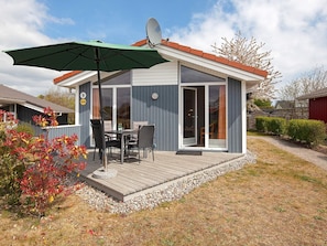 Ein modernes Haus mit einer Terrasse, einer Satellitenschüssel und einem Essbereich mit Gartenmöbeln.