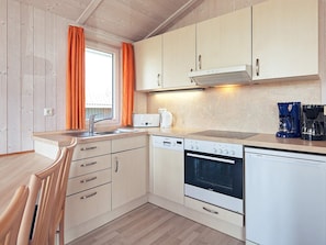 A compact kitchen with wooden cabinets, a built-in oven, a dishwasher, and a coffee maker. - Holiday Home in GrÃ¶mmitz (Groemitz)