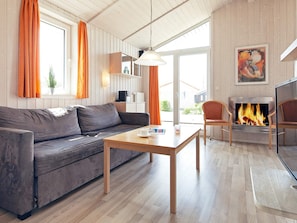 A cozy living room with a sofa, a wooden table, a fireplace, and a view through a glass door. - Holiday Home in GrÃ¶mmitz (Groemitz)