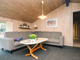 Una habitación acogedora con un sofá gris, una mesa redonda con tapa de mármol blanco y paredes de madera.