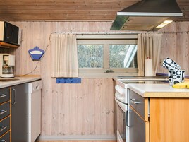 Una cocina compacta con paredes de madera, una ventana con cortinas, un microondas, una cafetera y una banana sobre la encimera.