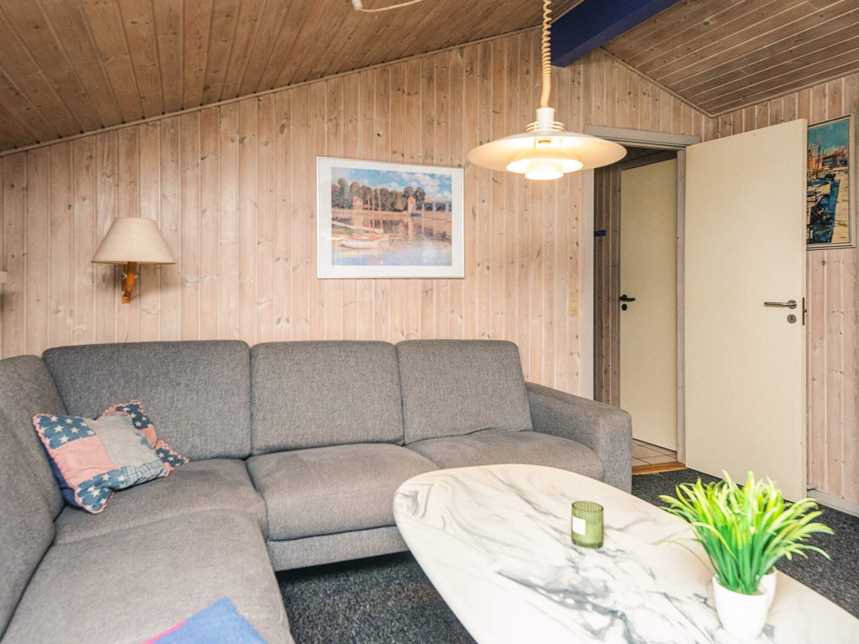 A room with a grey sofa, a marble coffee table, a green plant, a wall-mounted lamp, and a framed picture.