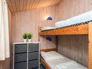 Une petite pièce comprenant un lit superposé, une petite commode blanche avec des tiroirs et une lampe fixée au mur.