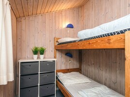 Una habitación compacta con una cama litera, un pequeño aparador blanco con cajones y una lámpara fijada a la pared.