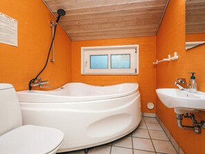 Un baño con una bañera blanca, un inodoro y un lavamanos. Hay una ventana con vista al cielo.