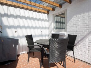 A patio with a table and chairs, a covered grill, and a white brick wall.