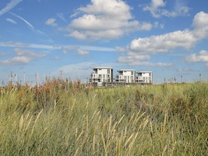 A modern building with multiple balconies, situated in a grassy area with a clear sky.
