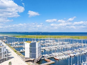 A marina with numerous boats docked, a modern building with a flat roof, and a clear view of the sea and distant land. - Holiday Home in Wendtorf (Schönberg)