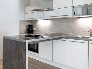 A modern kitchen with a central island, built-in oven, stainless steel sink, and white cabinetry. - Holiday Home in Wendtorf (Schönberg)