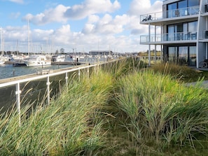 A marina with boats docked, a modern building with balconies, and a grassy walkway.