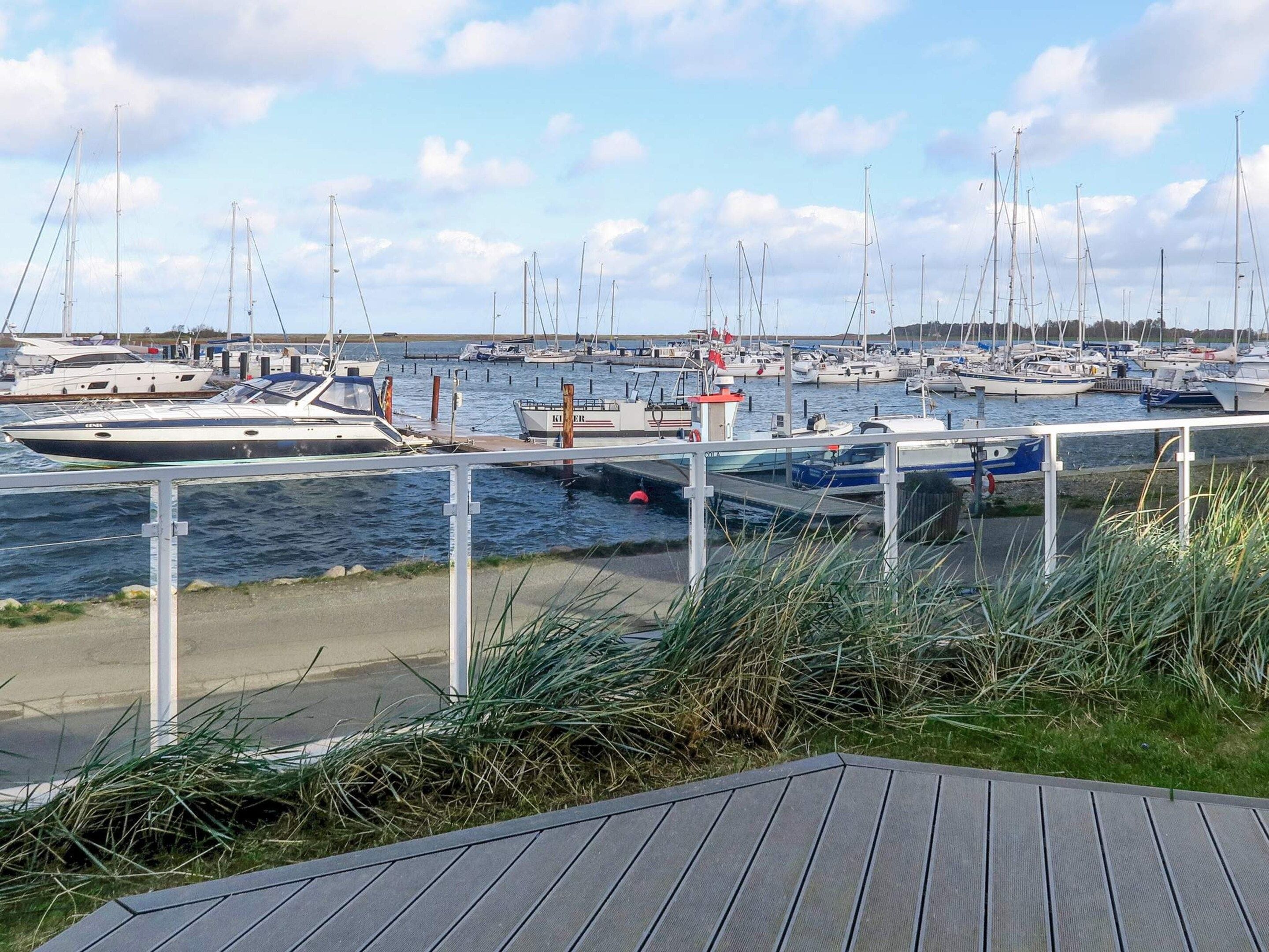 Un port de plaisance où sont amarrés de nombreux bateaux, une terrasse en bois au premier plan et un ciel dégagé.