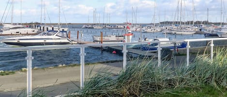 A marina with multiple boats docked, a wooden deck in the foreground, and a clear sky.