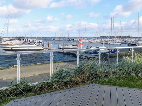 A marina with multiple boats docked, a wooden deck in the foreground, and a clear sky.
