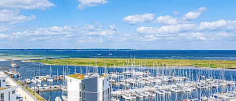 A marina with numerous boats docked, a modern building with a flat roof, and a clear view of the sea and sky.