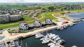 A marina with multiple boats docked, a modern building complex with a green roof, and a residential area in the background. - Holiday Home in Wendtorf (Schönberg)