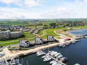 A marina with multiple boats docked, a modern building complex with a green roof, and a residential area in the background. - Holiday Home in Wendtorf (Schönberg)