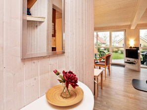 A room with a wooden interior, a dining area with chairs and a table, and a television mounted on the wall.