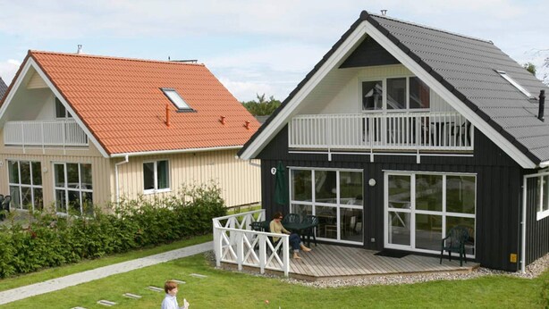 A two-story house with a deck, a red roof, and a large window.