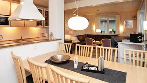 A modern kitchen with wooden cabinets, a dining area with a large table and chairs, and a cozy living space with a sofa and a TV.