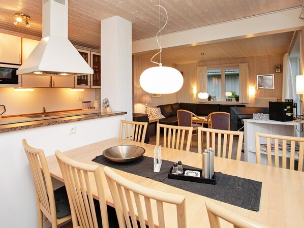 A modern kitchen with wooden cabinets, a dining area with a large table and chairs, and a cozy living space with a sofa and a TV.