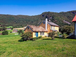 A two-story house with a thatched roof, surrounded by a grassy field and a forested hill. - 8 Person Holiday Home in Liabygda (Stranda)
