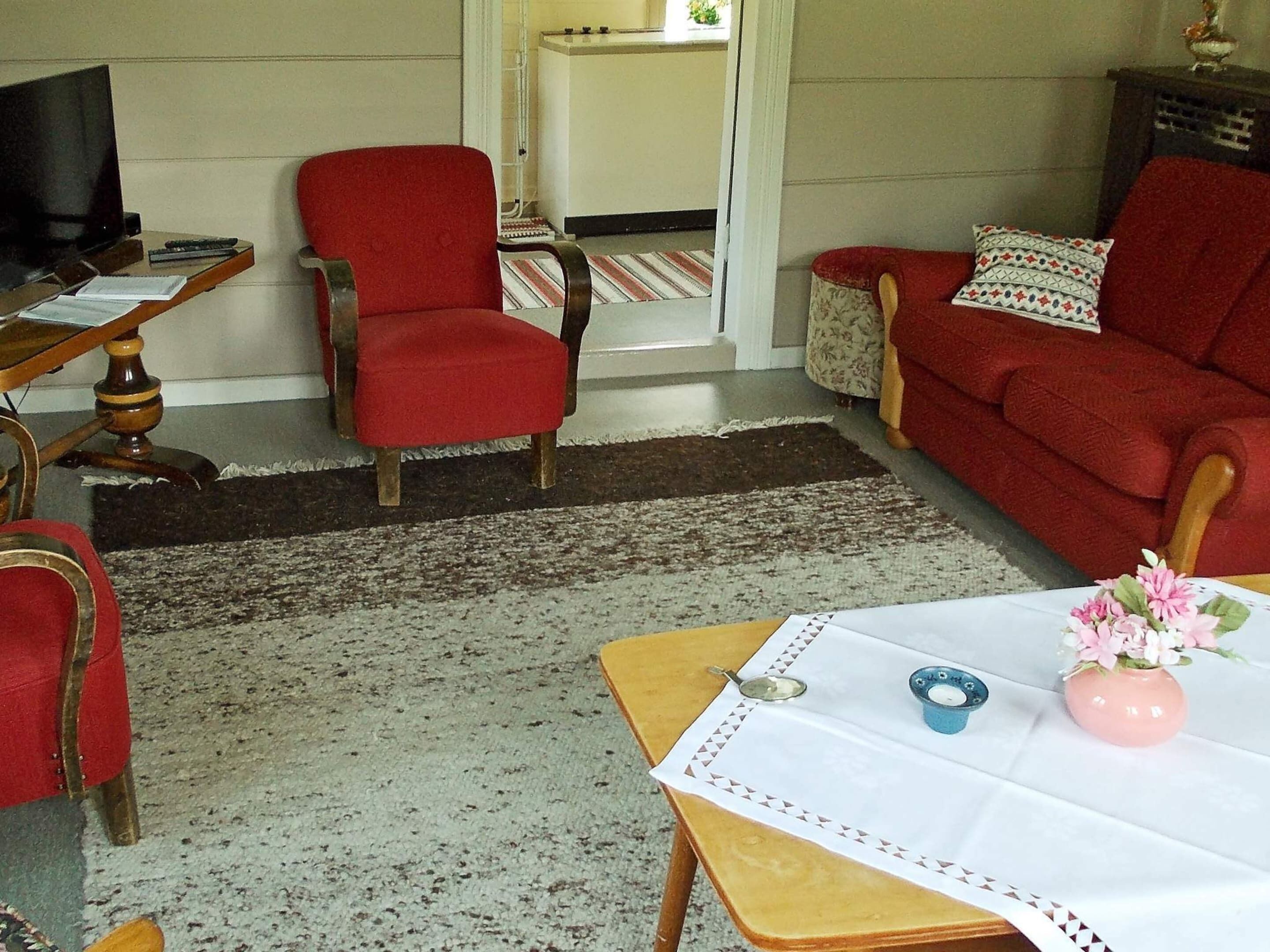 A living room with a red armchair, a sofa, a coffee table with a vase, and a television on a wooden stand.