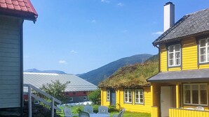 Ein gelbes Haus mit einem Reetdach, einem weißen Zaun und einer kleinen Terrasse mit weißen Stühlen und einem Tisch.