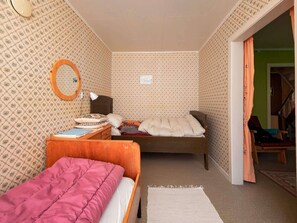 Une petite pièce chaleureuse, avec un papier peint à motifs, un lit en bois, un bureau doté d’un miroir et une chaise.