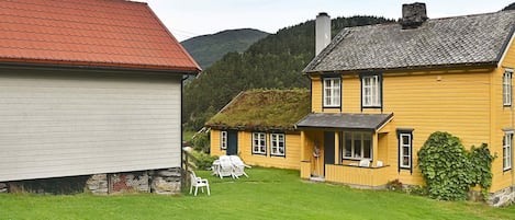 A rural house with a red roof, a yellow exterior, and a thatched roof extension.