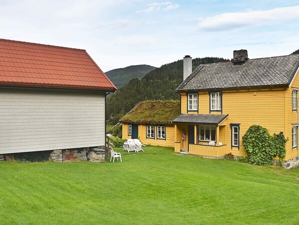 Une maison de campagne avec un toit rouge, une façade jaune et une extension de toit en chaume.