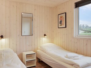 A room with wooden panel walls, a bed, a bedside table, a mirror, and a framed picture.