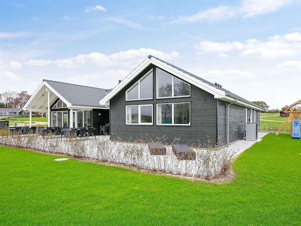 A modern building with a covered patio, large windows, and a grassy lawn.