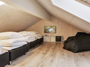 A bedroom with a sloped ceiling, a bed with pillows, a television on the wall, and a bean bag chair.